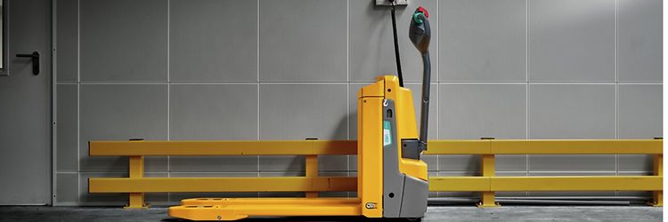 Żółty wózek widłowy unoszący (© Akumulatorowy wózek widłowy unoszący w magazynie.)