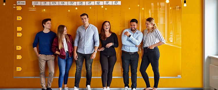 Gruppe junger Jungheinrich Mitarbeitender vor gelber Rückwand 