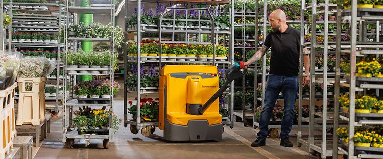  En gul Jungheinrich elektrisk truck bruges til at transportere planter i en butik.