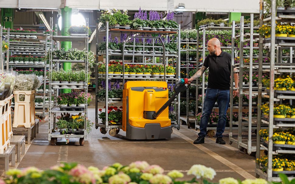  En gul Jungheinrich elektrisk truck bruges til at transportere planter i en butik.