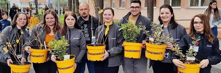 Photo of a group of people holding yellow Jungheinrich flowerpots with plants in them.