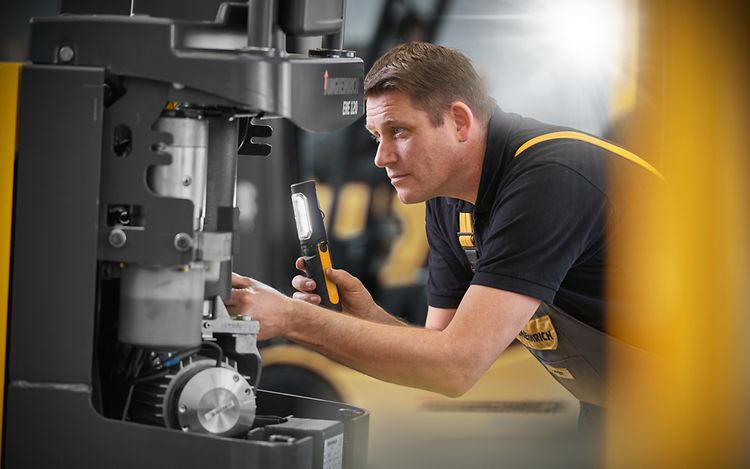 Photo shows a Jungheinrich employee using a flashlight to examine a part of the truck for refurbishment.