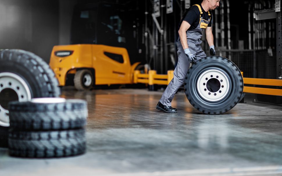 En tekniker från Jungheinrich rullar ett däck med en gul truck i bakgrunden.
