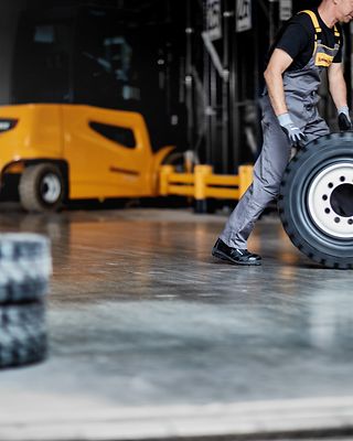 En tekniker från Jungheinrich rullar ett däck med en gul truck i bakgrunden.