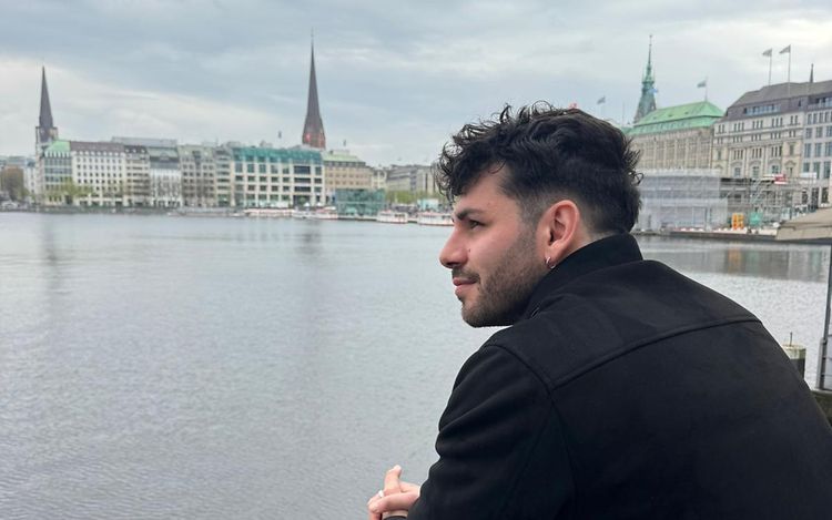 Pietro steht an der Binnenalster in Hamburg, lehnt auf einem Geländer und schaut in die Ferne.