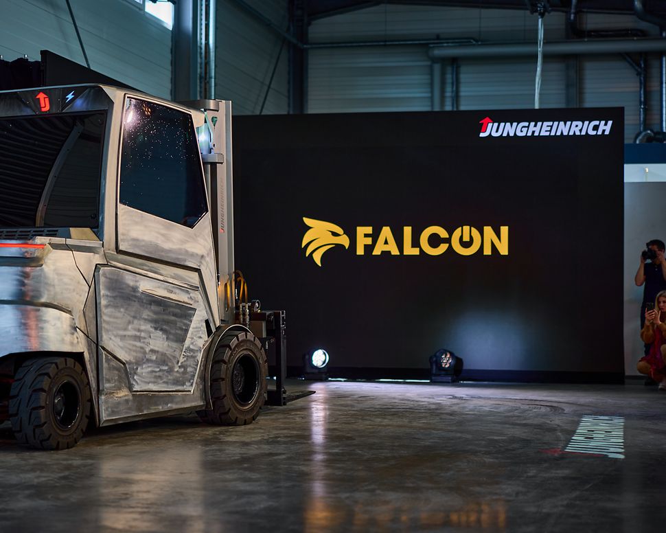 A grey forklift truck is parked in front of a black screen bearing the yellow lettering ‘Falcon’.