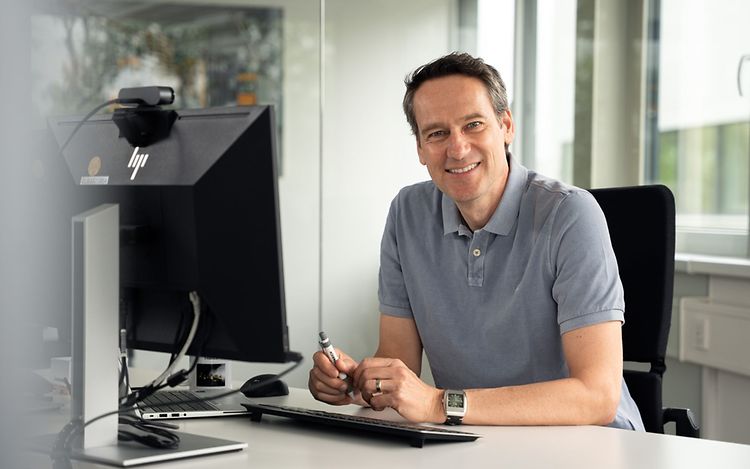 Dr Tobias Harzer is sitting at a desk, smiling at the camera.