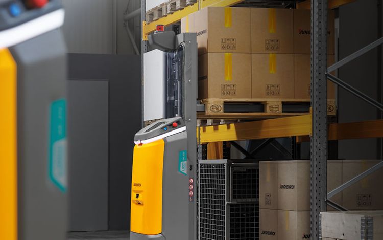 An autonomous forklift truck is standing in front of a rack and is lifting a pallet of stacked boxes onto it.