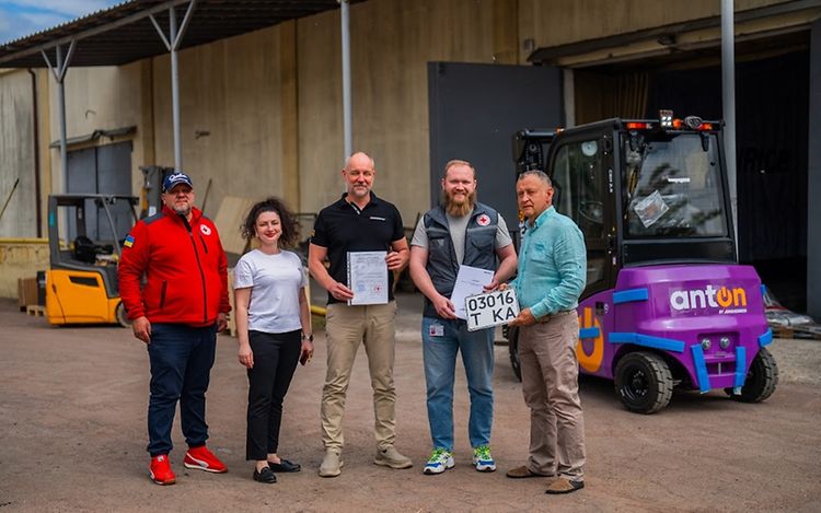Five people are standing in the centre and looking at the camera. In the background are two Jungheinrich forklift trucks.