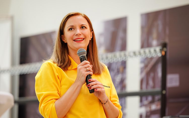 Marta Janukowicz is holding a microphone and gazing into the distance.