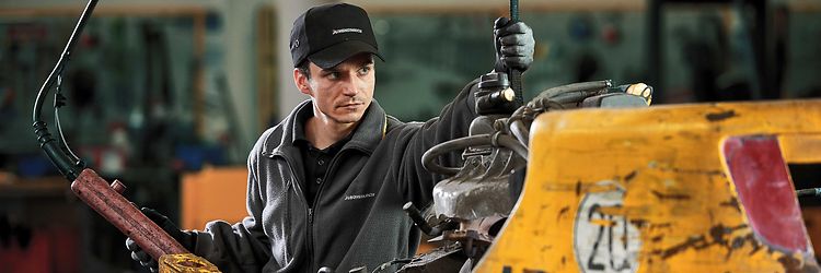 A man is using a machine to lift a vehicle that shows signs of heavy use.