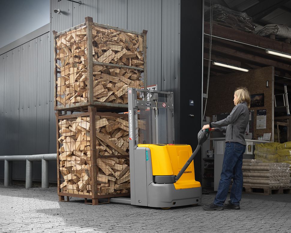 A woman is pushing a forklift truck loaded with baskets containing logs.