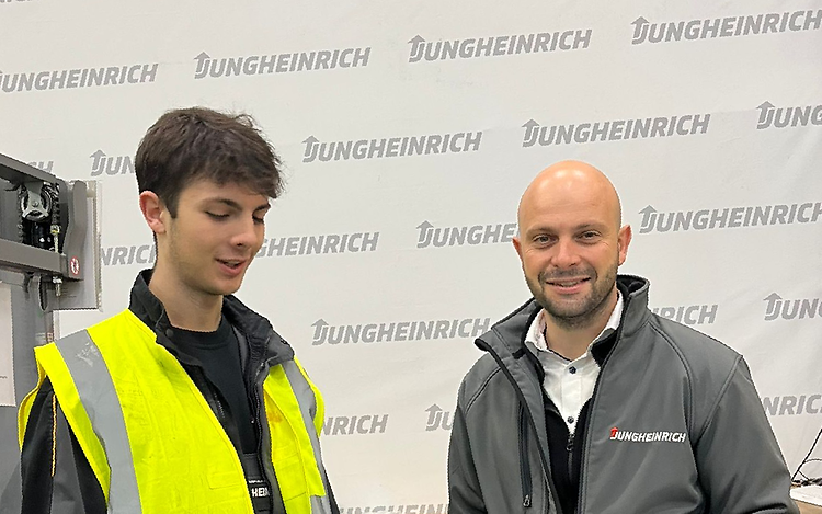 Milan and Wladimir Iliev are standing in a factory. Milan is wearing a high-visibility vest and Wladimir is holding a laptop.