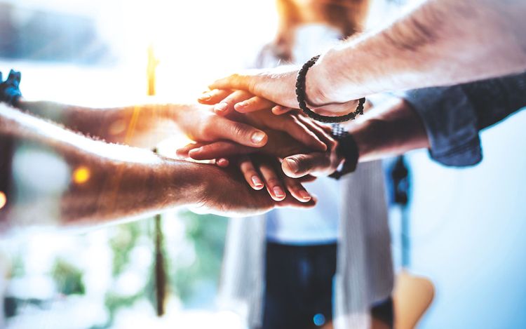 Seven hands are placed on top of one another in the centre of the picture.