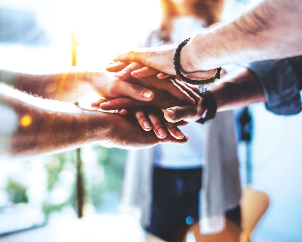 Seven hands are placed on top of one another in the centre of the picture.