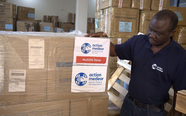 Ein Mitarbeiter von action medor steht neben Kisten mit dem Aufdruck "Nothilfe Ebola".