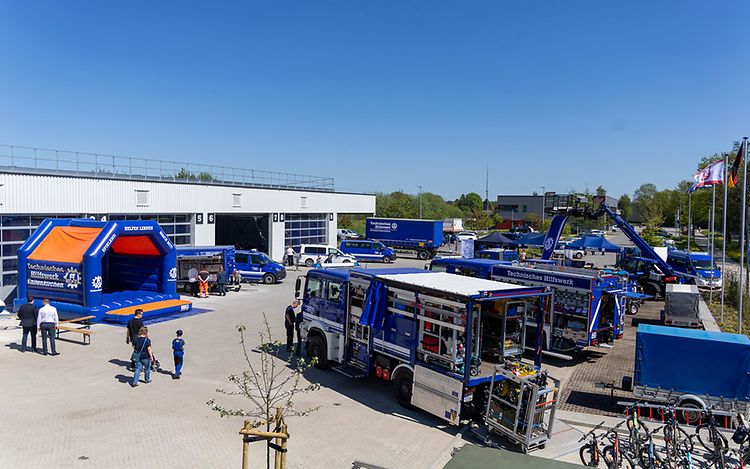 Several blue THW vehicles are parked on a site. On the left of the picture is a blue THW bouncy castle.