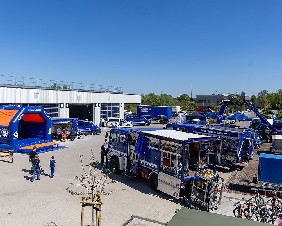Several blue THW vehicles are parked on a site. On the left of the picture is a blue THW bouncy castle.