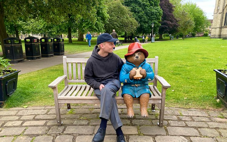 Mats sitzt auf einer Parkbank neben einer Skulptur von Paddington Bär.