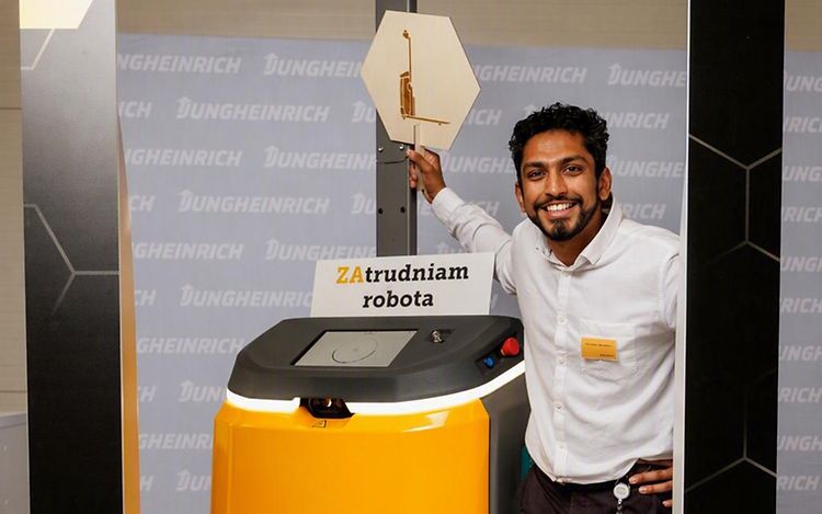 Uzair Mukadam steht neben einem gelben autonomen Mobile Robot und lächelt in die Kamera.