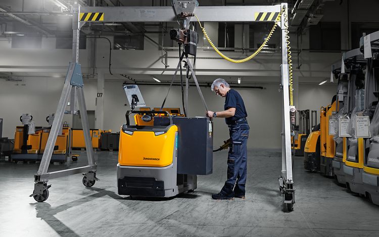 Im Zentrum des Bildes steht ein Mann, der mithilfe eines Gerüsts eine Batterie in ein Jungheinrich Fahrzeug einbaut.