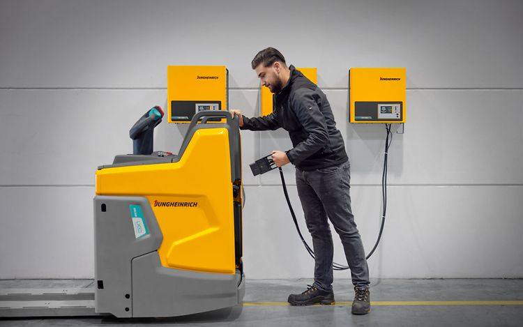 A man dressed in black is connecting a Jungheinrich vehicle to a charger.